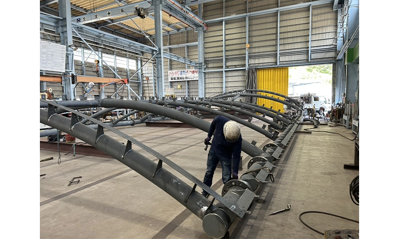 工場内で建築用鉄骨の大型部材を組み立てる鉄骨製作作業の様子