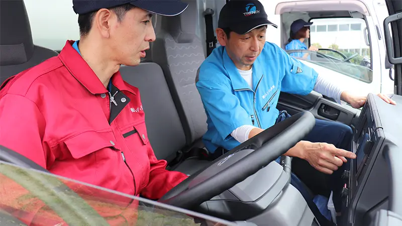 トラック運転席で操作方法を指導するスタッフ